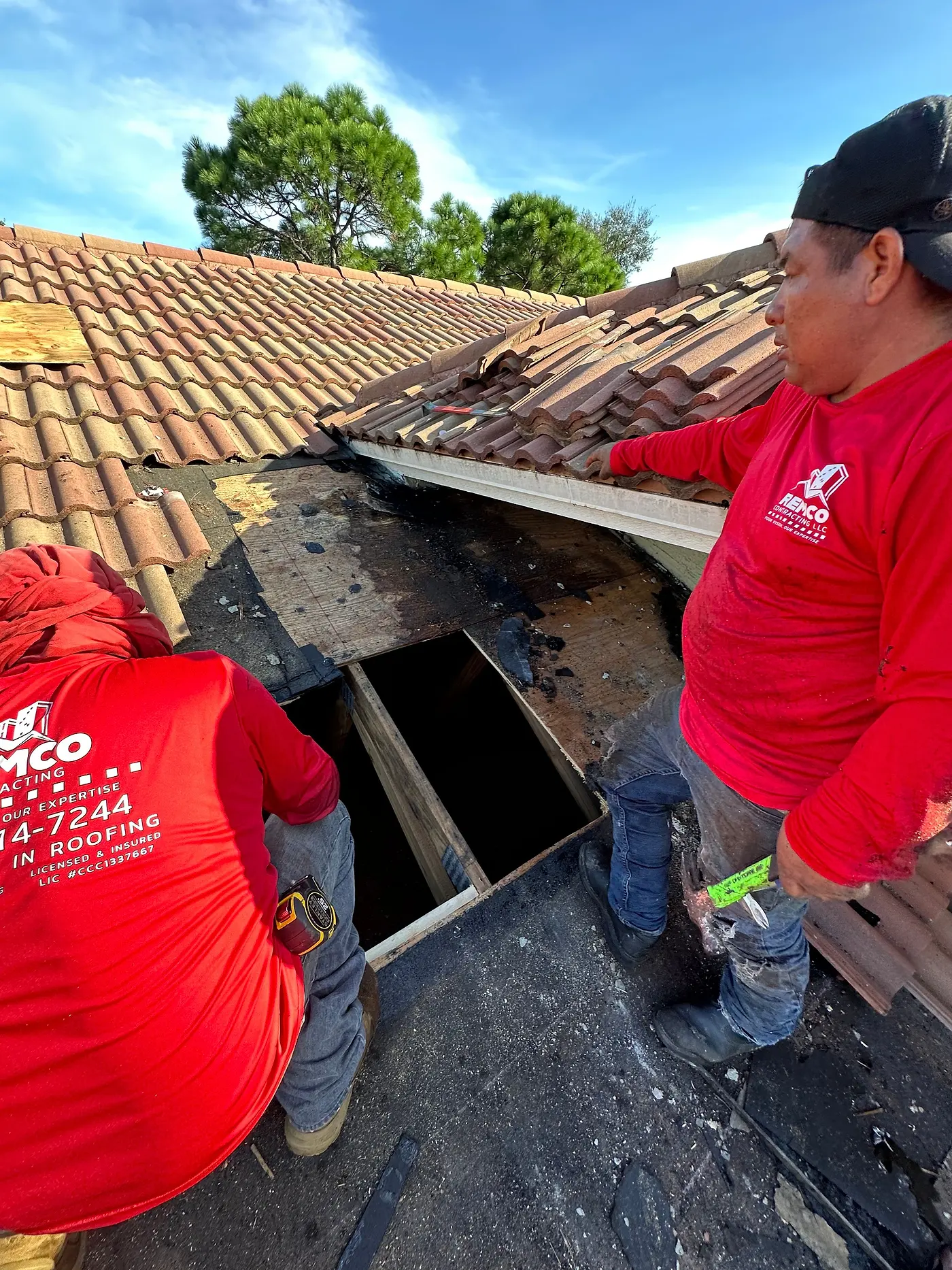 Two Remco roofers repairing rotted decking under a tile roof